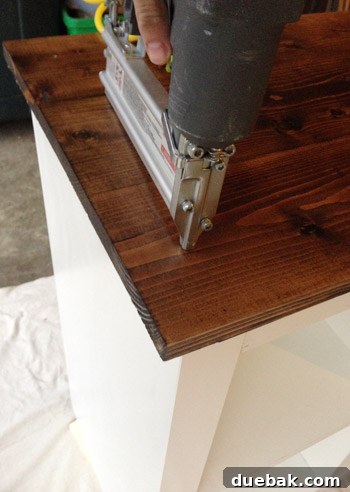 Using a nail gun to attach the wood panels to the Expedit.