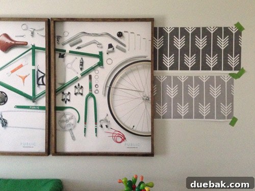A mobile phone photo showing two large wallpaper samples taped side-by-side on a nursery wall with bike prints, testing placement.