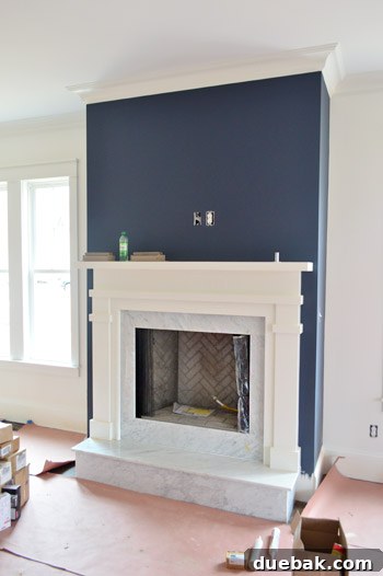 Close-up of a fireplace with a white mantel, marble surround, and herringbone brick.