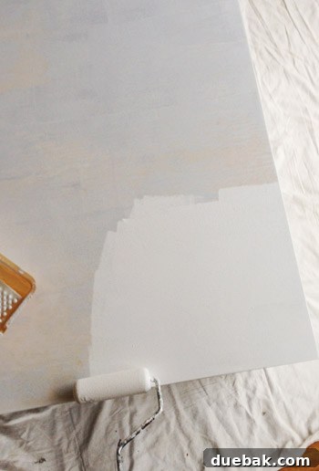 Applying Benjamin Moore Simply White Advance paint to the desk with a foam roller.