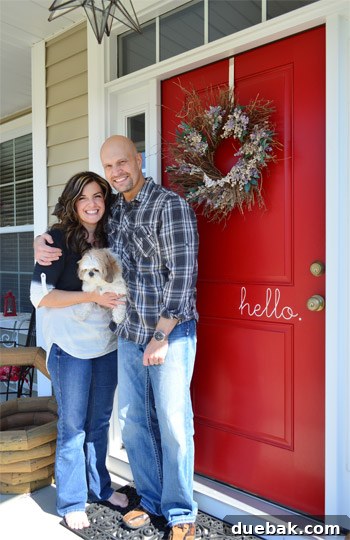 Becky and Brian at their Heritage Red front door, featuring a festive wreath and a friendly 'Hello' decal, welcoming guests to their charming home.