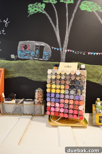Tabletop paint display case made of wire sits on a desk crafted from an old door, with a charming chalkboard camper drawing behind it, showcasing creative organization.