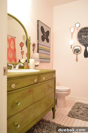 Farmhouse green bathroom vanity, repurposed from a dresser, features a striking collage of vintage mirrors elegantly arranged on the wall above.
