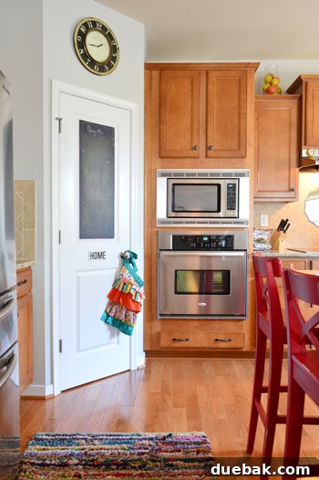 Kitchen features warm wood cabinets and a corner pantry with a functional chalkboard door, adding a personalized touch to the space.