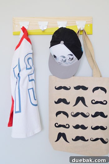 A boys' bedroom with a white wall and a wooden hook rail featuring a yellow diagonal stripe on the bottom, with items hanging on it.