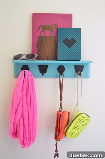 A girls' bedroom featuring a blue painted wall, a wooden hook rail with a ledge, and various items hanging on mix-and-match ORB hooks.
