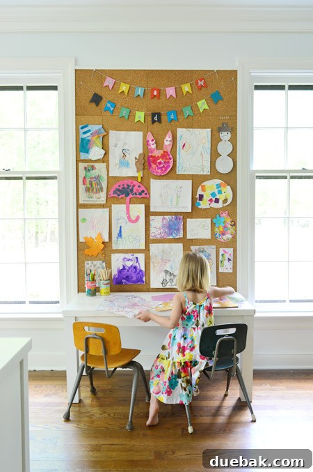 kids art displayed on large cork board wall in home office above kids art desk