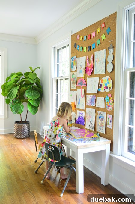 child working on art below giant cork board wall with drawings and painting pinned up