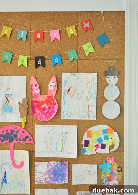 close up detail of kids art hung on cork board wall including name banner bunting from etsy