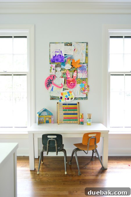 small fabric covered cork board used to pin up kid art projects above small homemade desk and schoolhouse style chairs