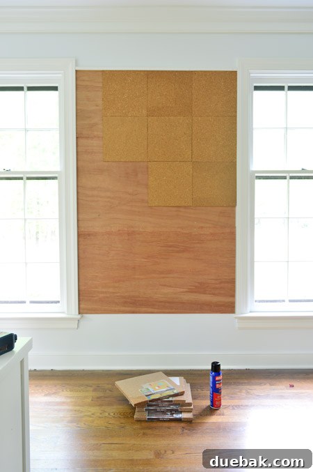 applying cork tiles to wall to create oversized cork board wall in kids art area