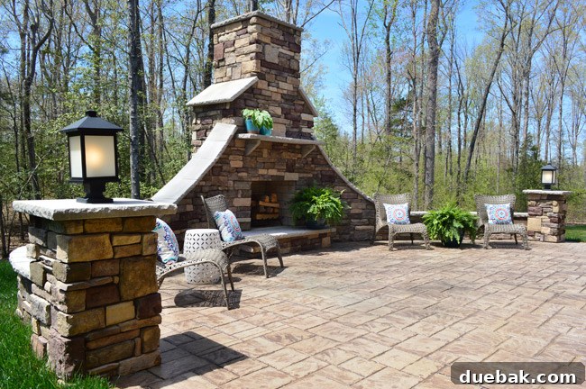 Stamped concrete patio with a large stone outdoor fireplace, framed by the house.