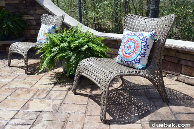 Casual seating area on the patio with woven lounge chairs and planters from Lowe's, facing the stone fireplace.