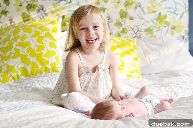 Big Sister Photo With Newborn Baby Brother In Front Of Colorful Background Fabric