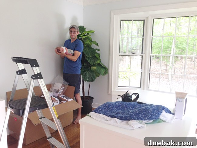 John Holding Infant Son On Arm In DIY Newborn Photo Shoot