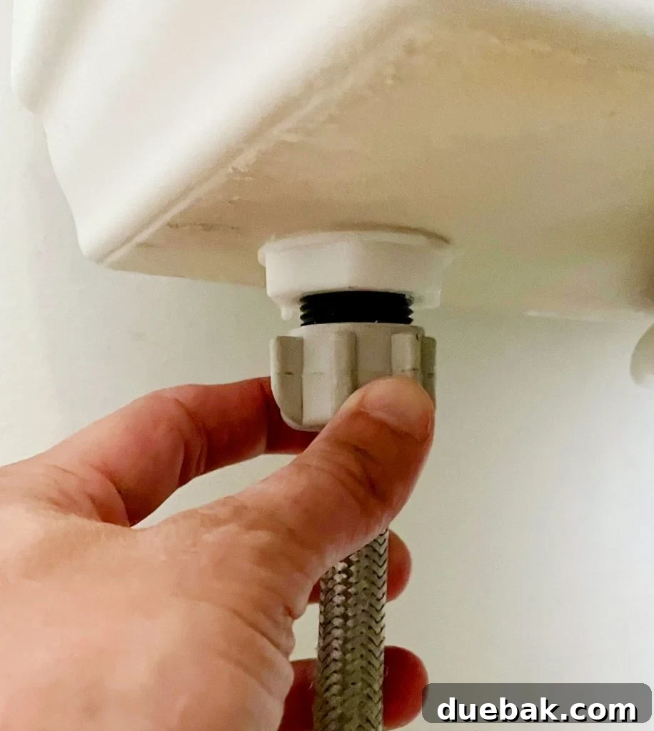 Hand Loosening Water Supply Line Under Toilet Tank