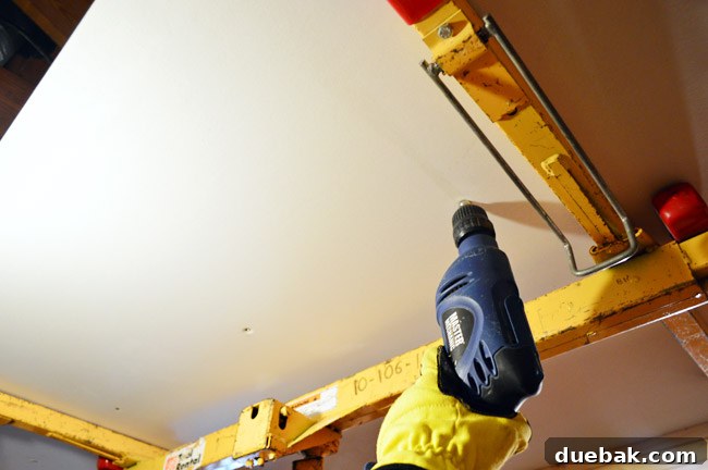 attaching drywall sheet to the ceiling using a drill