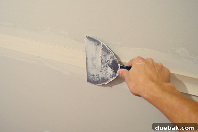 drywall knife smoothing tape into drywall tape and bottom layer of mud