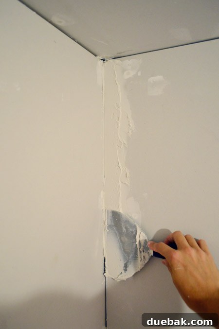 flat drywall knife putting joint compound into corner of room