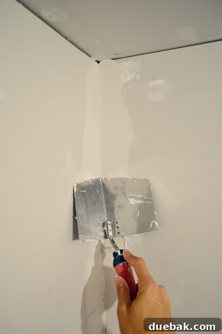 corner trowel smoothing thick first layer of drywall mud in room corner
