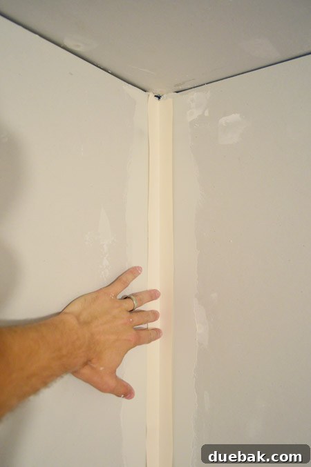 handing pressing drywall tape into corner layer of mud