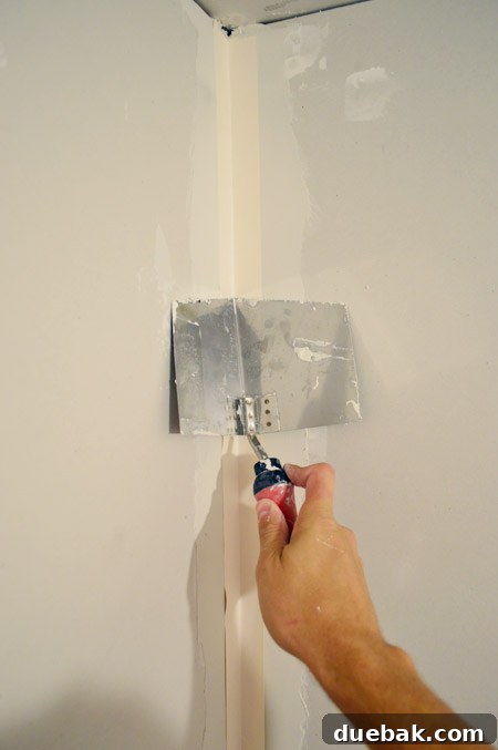 corner trowel pressing tape into corner of drywalled room