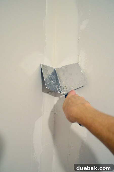 John smoothing drywall mud in corner of room using corner trowel