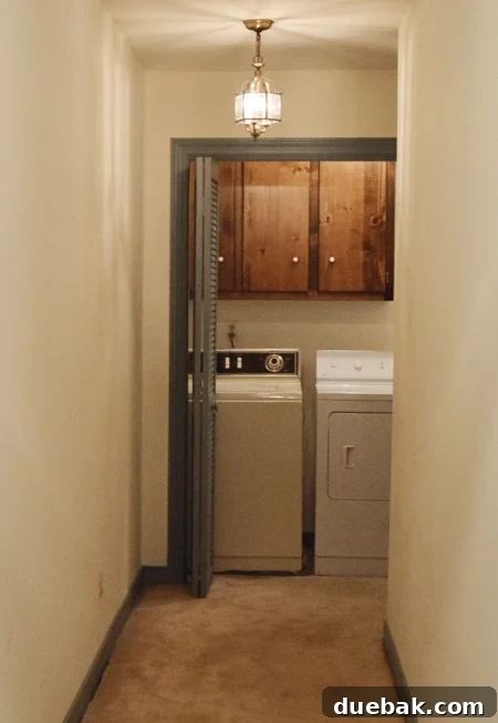Bonus Room Glow Up 20 Dated laundry room closet at end of a hall with bifold doors, dark cabinets, carpet, and mismatched old washer and dryer