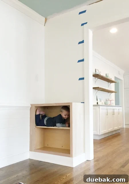 Tailored Book Nooks DIY Built Ins 13 A base cabinet with newly installed baseboard trim and a playful toddler, showcasing the progress of the built-in bookshelf project