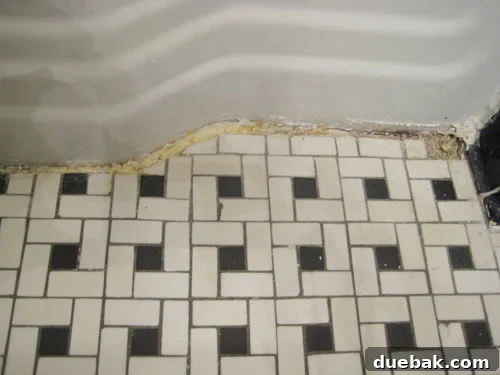 The Secret to Flawless Caulk Lines 3 Close-up of a hand using a box cutter to carefully remove old, dirty caulk from a bathroom tile edge