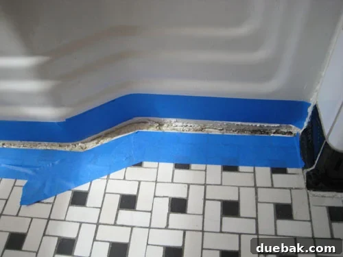 The Secret to Flawless Caulk Lines 4 Hand applying painter's tape along a bathroom tile edge, preparing the surface for new caulk application