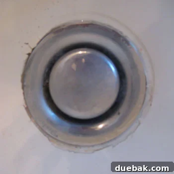 The Secret to Flawless Caulk Lines 6 Close-up of a dirty and corroded bathtub drain before revitalization, showing worn glaze and grime