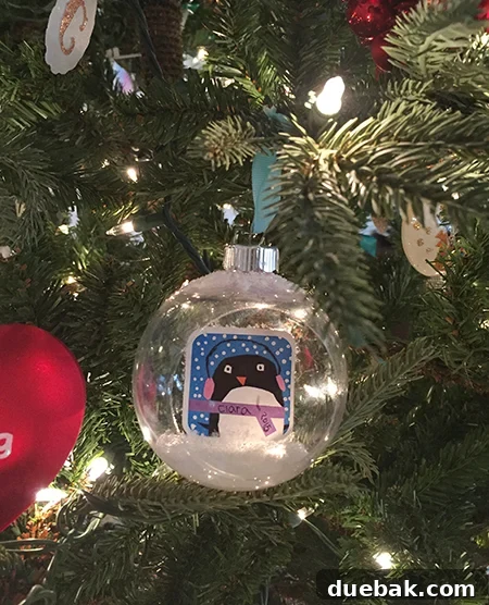 Close-up of a clear plastic dome ornament with a child's blue bird drawing inside, decorated with fake snow.