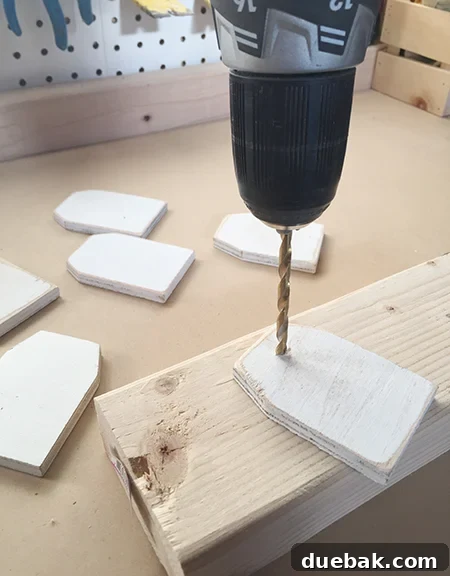 Drilling a small hole into a wooden tag ornament with a power drill and a piece of scrap wood for protection.
