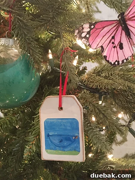 Threading a red ribbon through the hole of a wooden tag ornament with a child's art sticker.