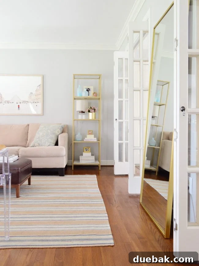 Bright, neutral living room after a budget-friendly makeover, featuring gold accents, a large Paris art piece, and clear ghost chairs, exuding modern elegance.