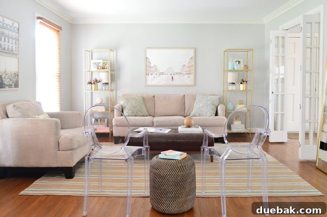 Transformed neutral living room after a budget-friendly makeover, showcasing gold shelves, large Paris art, clear accent chairs, and a leaning mirror.