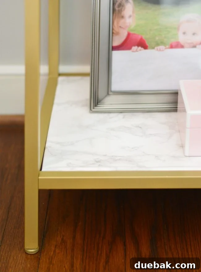 Close-up of an IKEA metal shelf transformed with gold spray paint and marble contact paper, highlighting the custom aesthetic and decorative items.