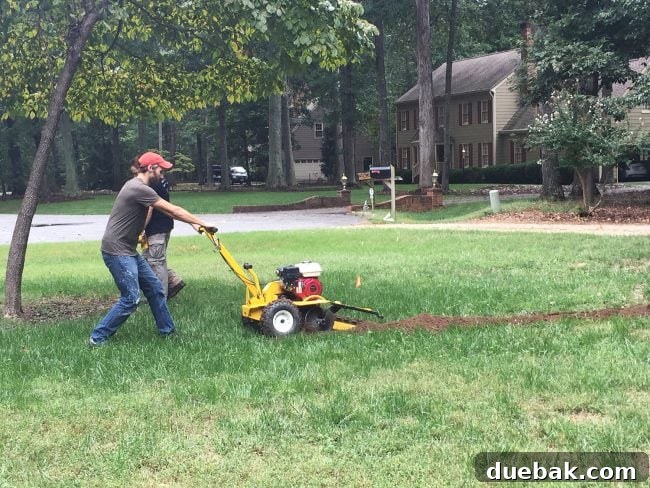 Individual using a trencher tool to dig irrigation system trenches across a front yard