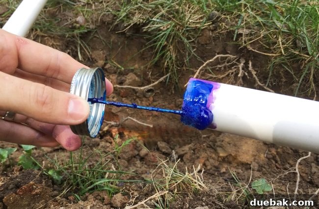 Applying blue PVC cement to the end of an irrigation system pipe before connection