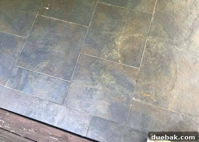 A corner of the outdoor tile floor, heavily soiled with dirt and grime, before pressure washing.