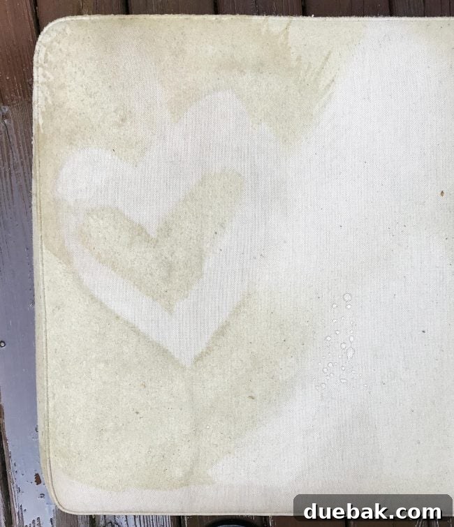 A large outdoor sofa cushion after pressure washing, showing a heart-shaped clean spot and dramatic overall improvement.