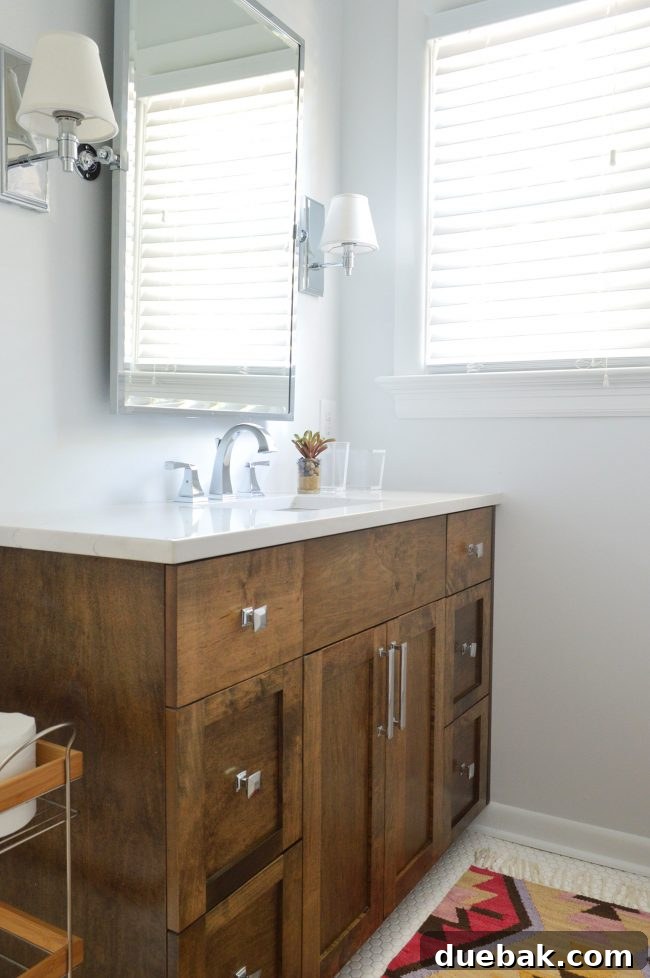 Elegant master bathroom with wood vanity, white hex tiles, and colorful rug