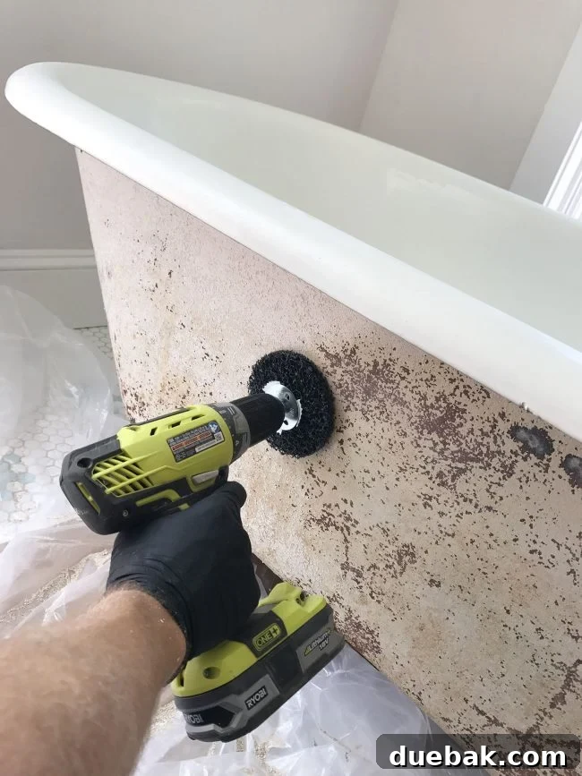 Rust-removing sanding attachment on a drill actively buffing the outside of an old clawfoot tub