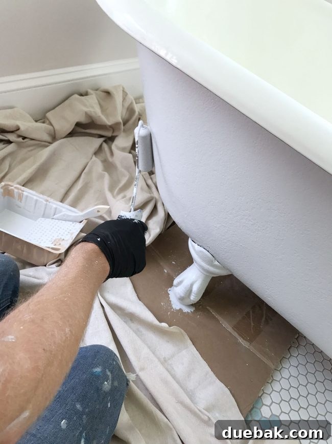 Applying primer to a clawfoot tub using a small foam roller, demonstrating painting technique
