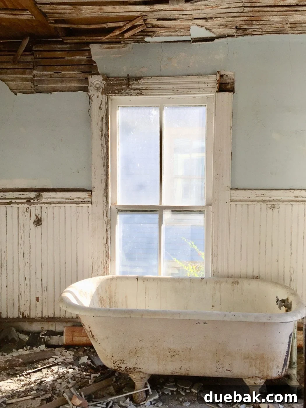 Before photo of a beach house bathroom featuring crumbling walls and a visibly dirty clawfoot tub