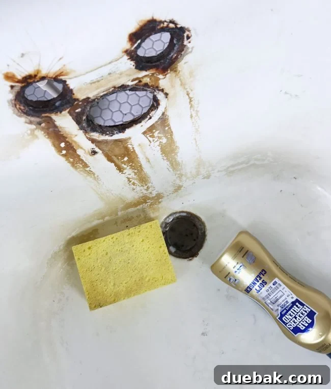 Sponge and Bar Keeper's Friend cleanser applied to a rust-stained clawfoot tub
