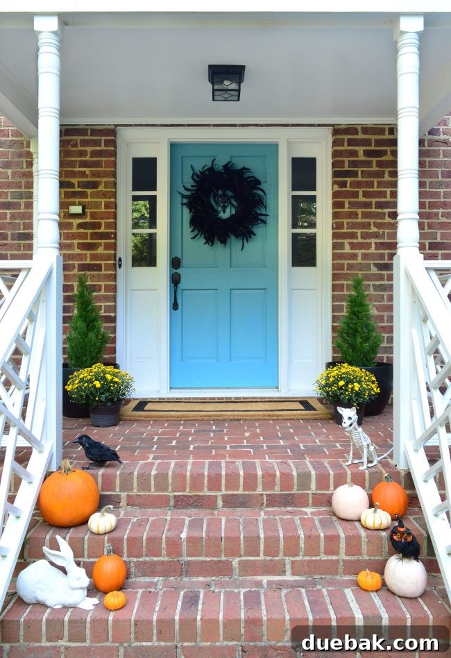 Front porch decorated for Halloween with pumpkins, a blue door, and mums