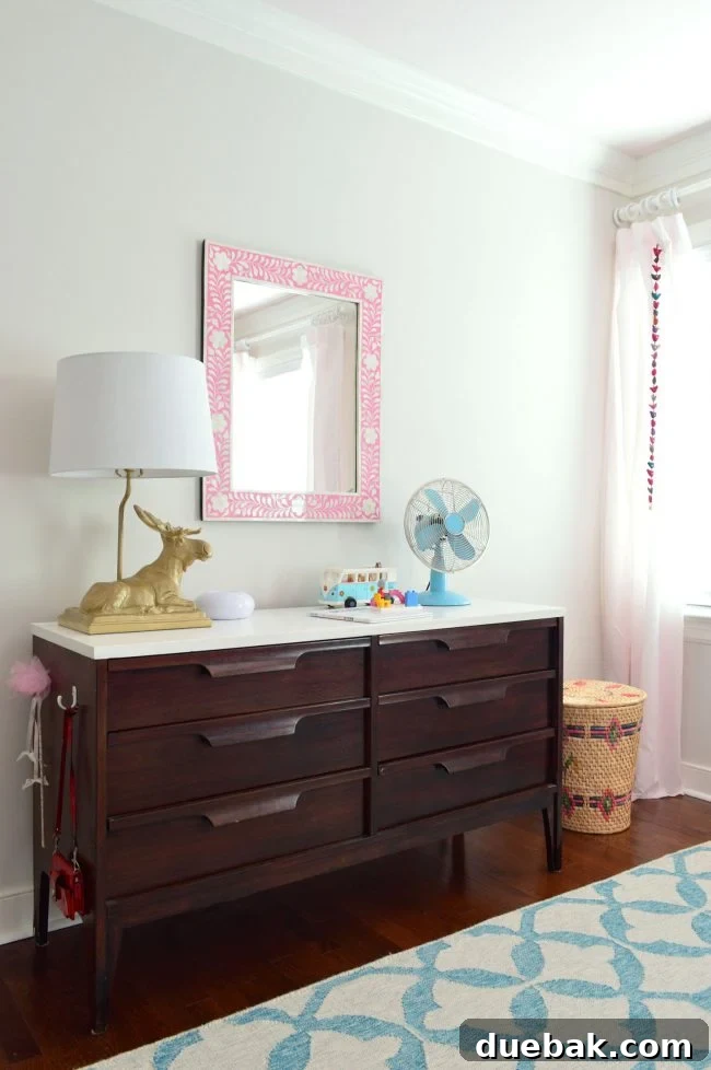 Girls bedroom featuring a midcentury dresser, pink inlay mirror, and new paint color