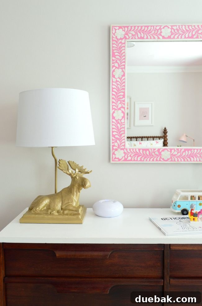 Girls bedroom with golden moose lamp, pink mirror, and neutral wall color